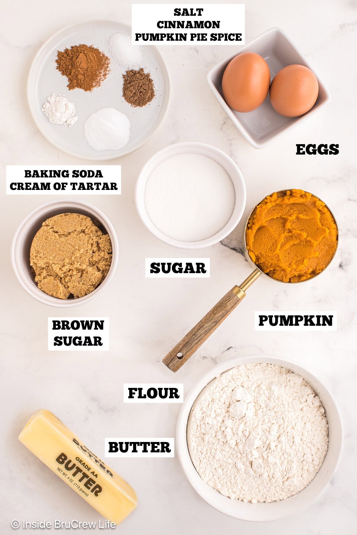 A white board with bowls of ingredients needed to make pumpkin cookies.