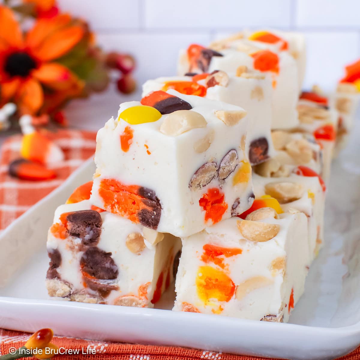 A white tray stacked with white chocolate candy corn fudge.