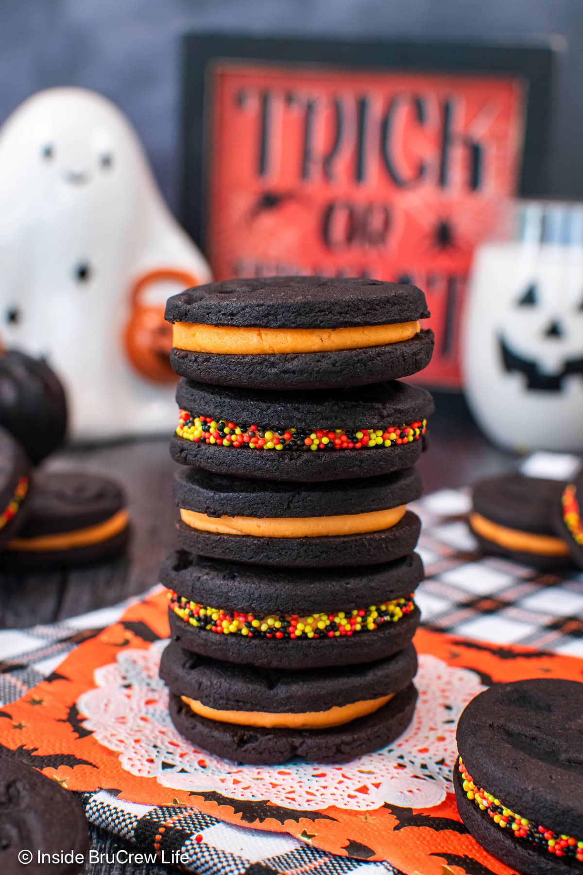 A stack of 5 halloween cookies with orange filling and sprinkles.