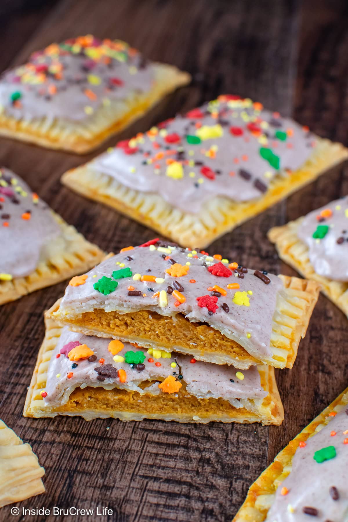 Two halves of pumpkin pie pop tarts stacked on a wood board.