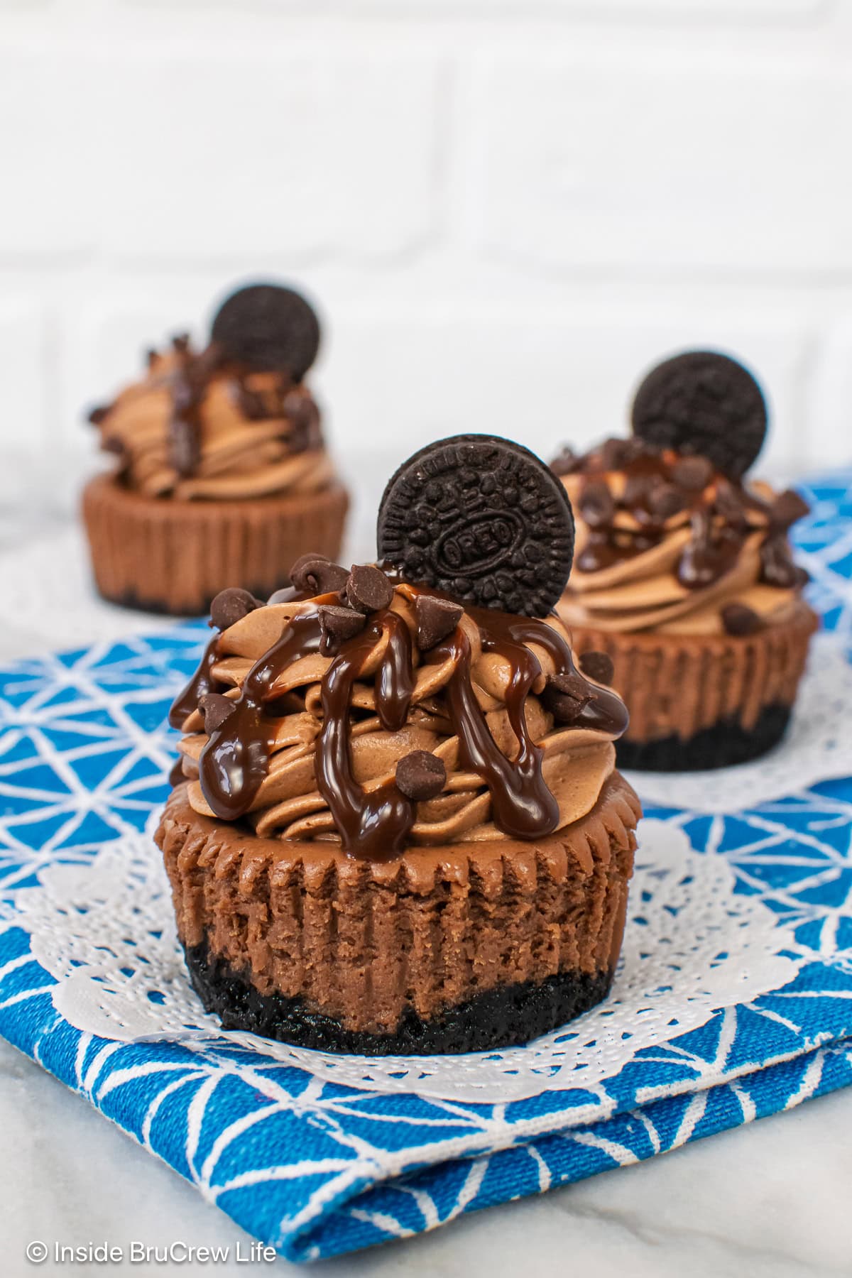 Three small dark chocolate cheesecakes on a white and blue towel.