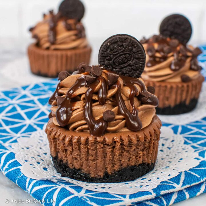 Three small dark chocolate cheesecakes on a white and blue towel.