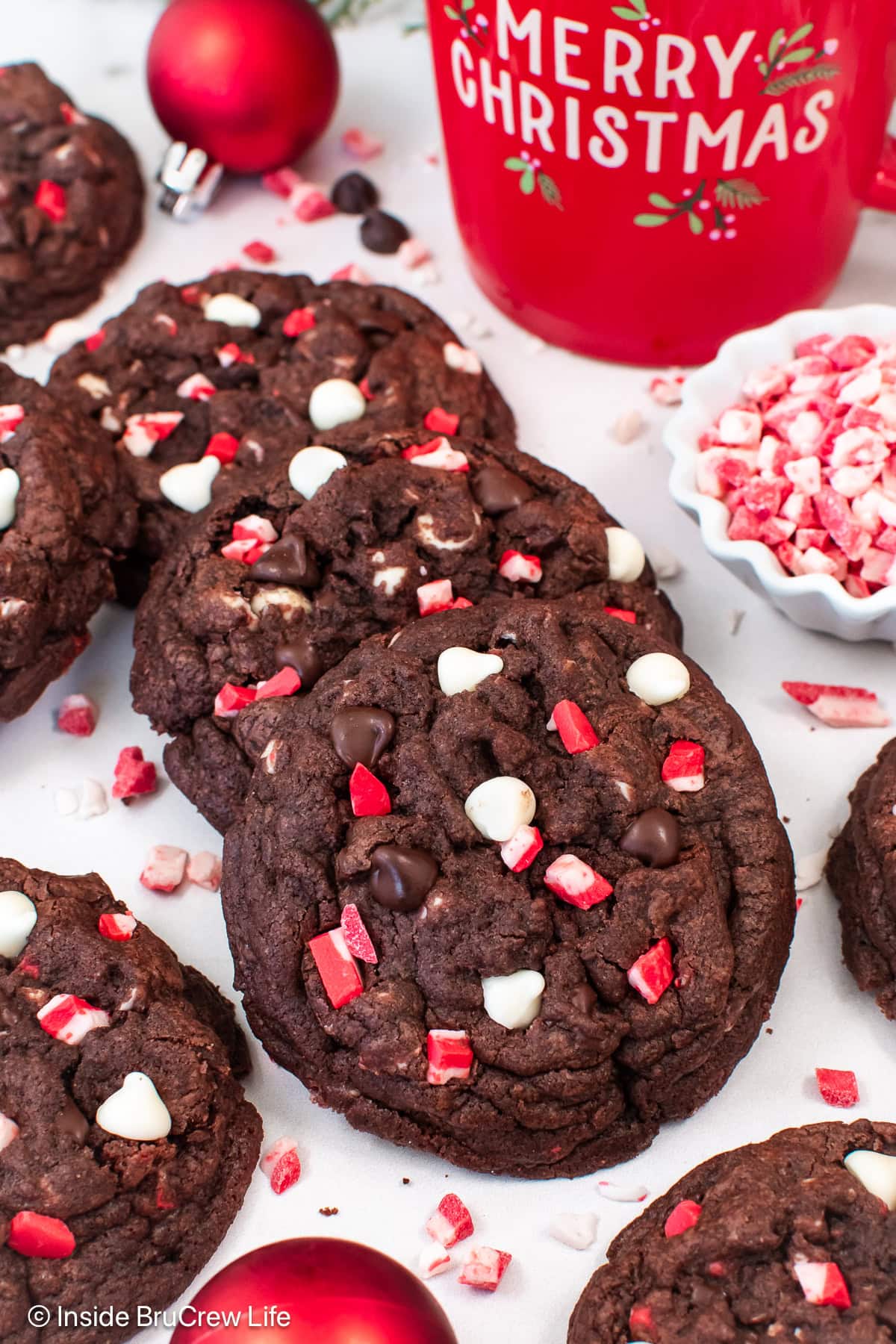 Three chocolate peppermint chip cookies on a white board.