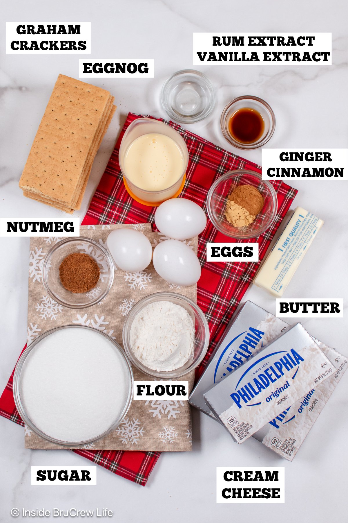 A white board with bowls of ingredients needed to make cheesecake with eggnog.