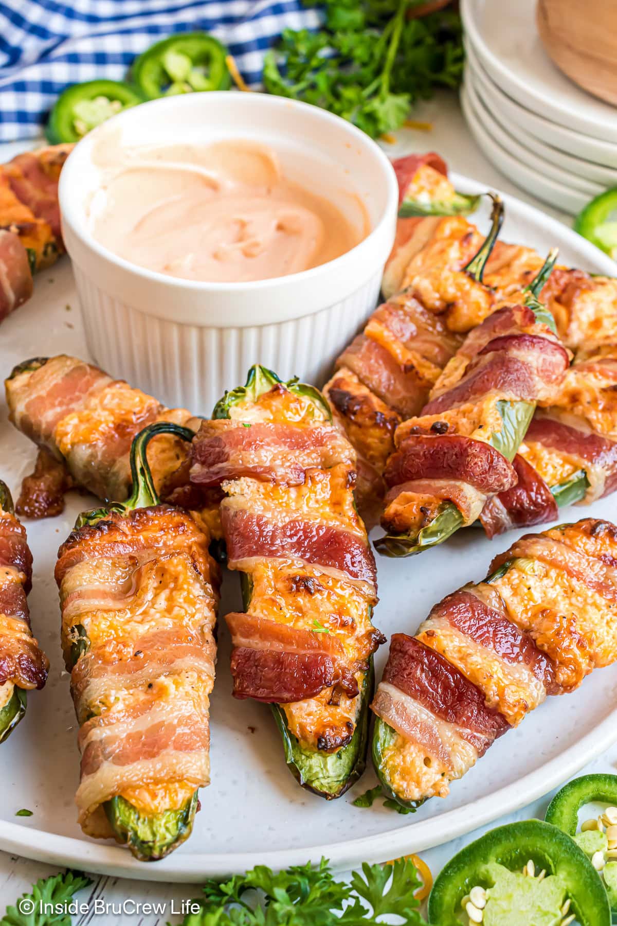 Bacon wrapped jalapenos on a white plate with a bowl of dip.