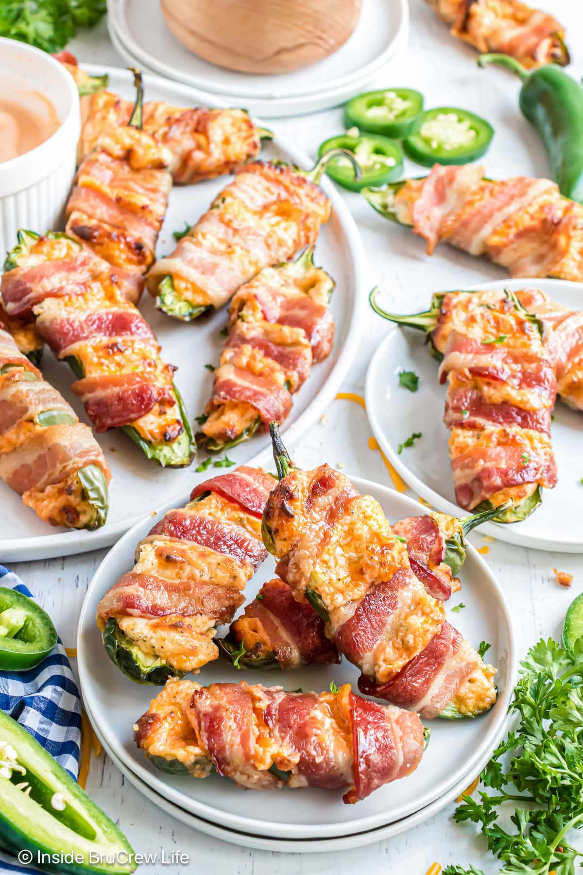 A table covered with white plates filled with bacon wrapped jalapeno poppers.