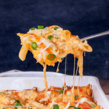 A scoop of cheesy pasta being lifted out of a casserole dish.