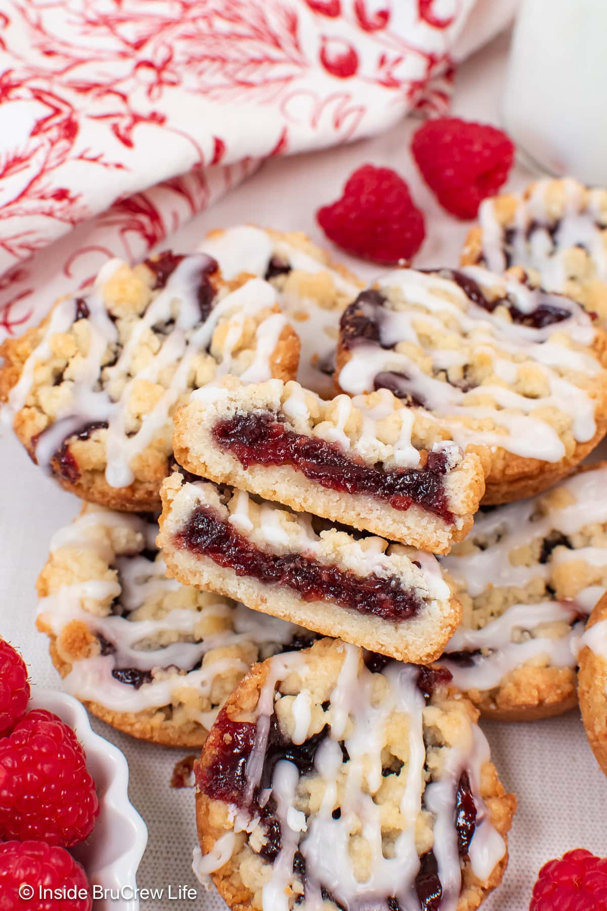 A pile of raspberry cookies with one cut in half so you can see the filling.