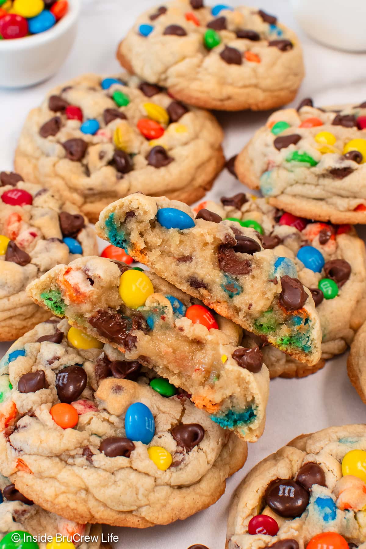 A pile of M&M chocolate chip cookies in a pile with one cut in half.