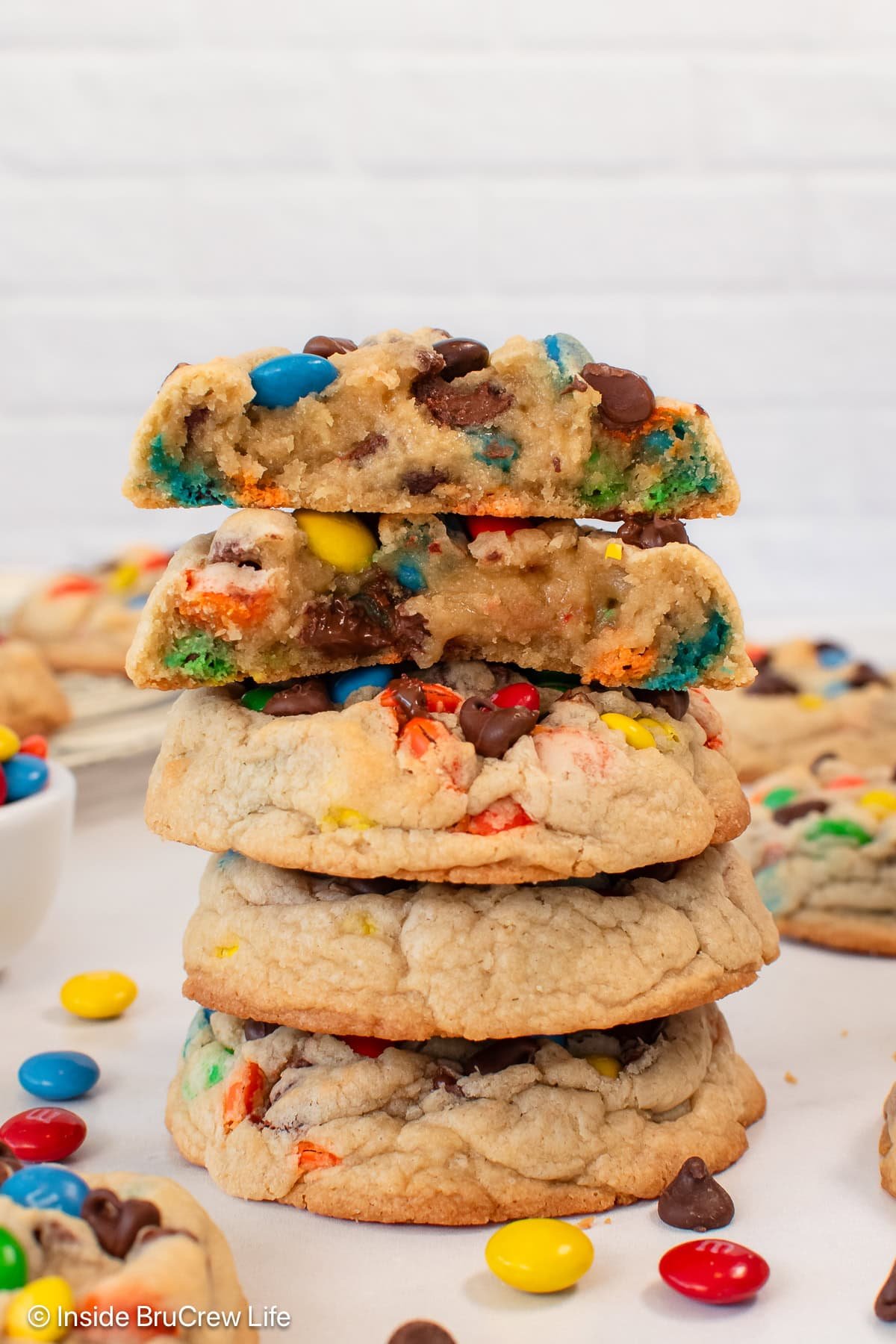 A stack of M&M cookies with one cut in half on top showing the gooey center.