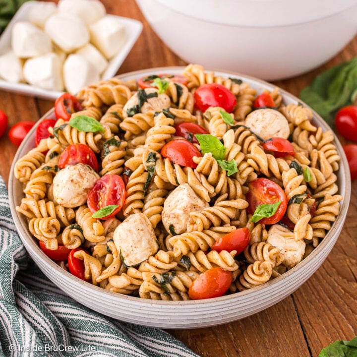 A bowl of Caprese pasta salad on a brown board.
