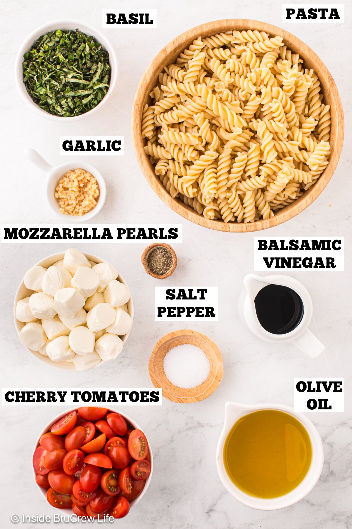 A white board with bowls of ingredients needed to make a Caprese pasta salad.