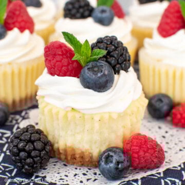 Vanilla cheesecakes topped with whipped cream and berries on a white paper.