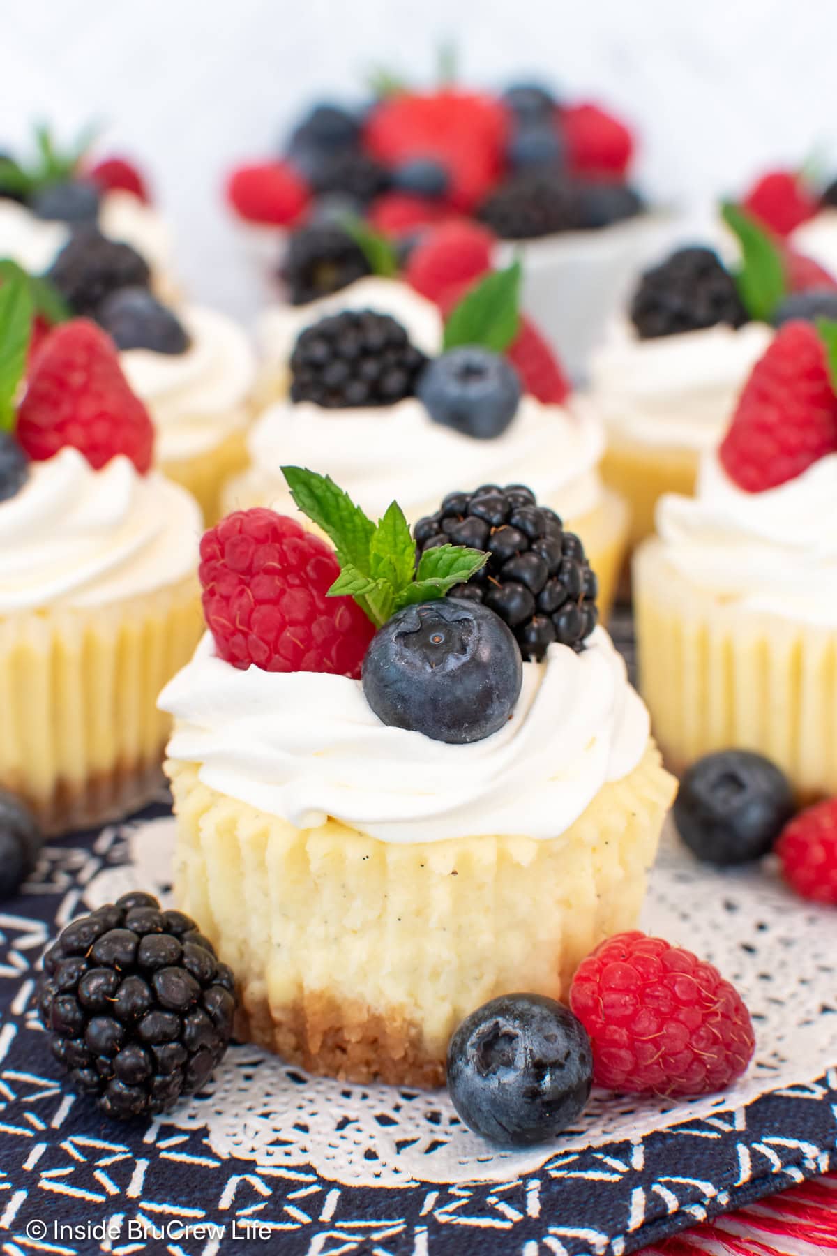 Vanilla cheesecakes topped with whipped cream and berries on a white paper.