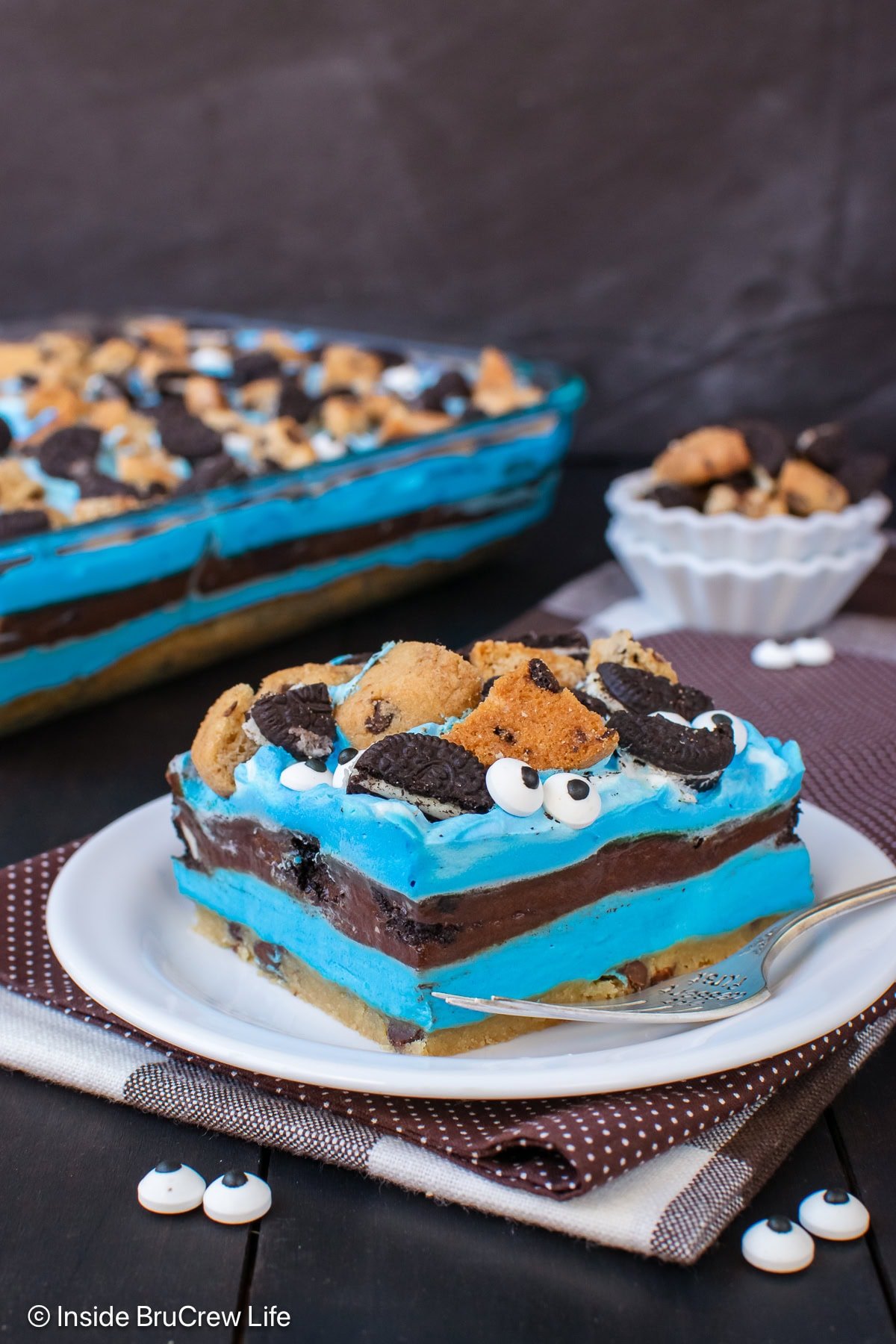 A slice of cookie monster layered dessert with extra cookies on a white plate.