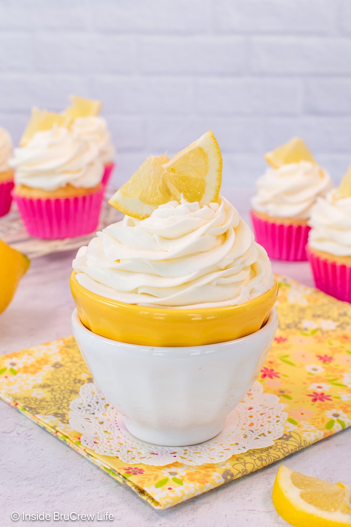 A bowl filled with a swirl of lemon buttercream and lemon wedges.