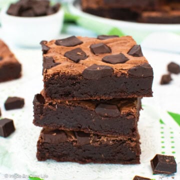 Three chocolate brownies stacked on a white board.