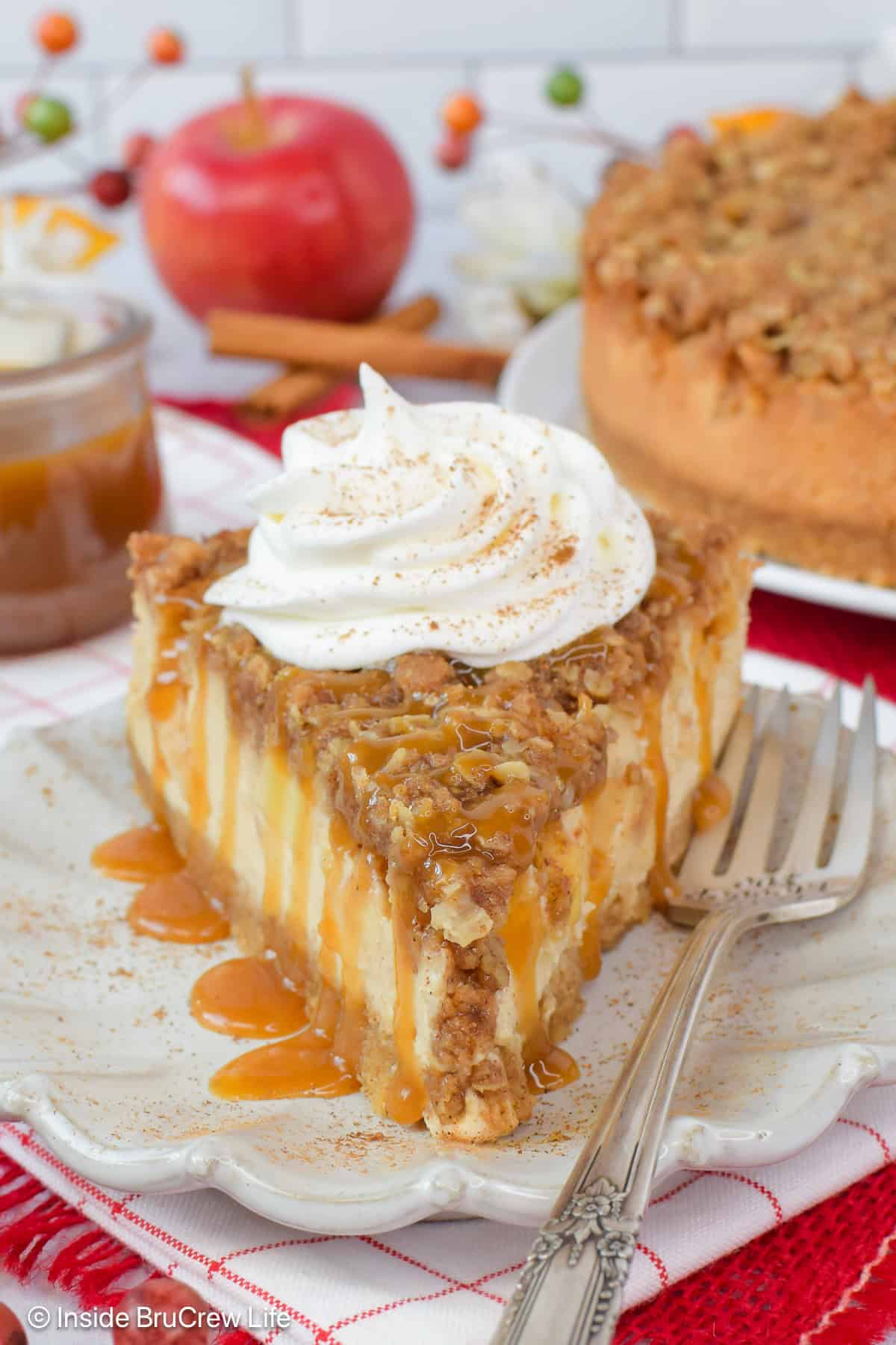 An apple crisp cheesecake slice with caramel and whipped cream.