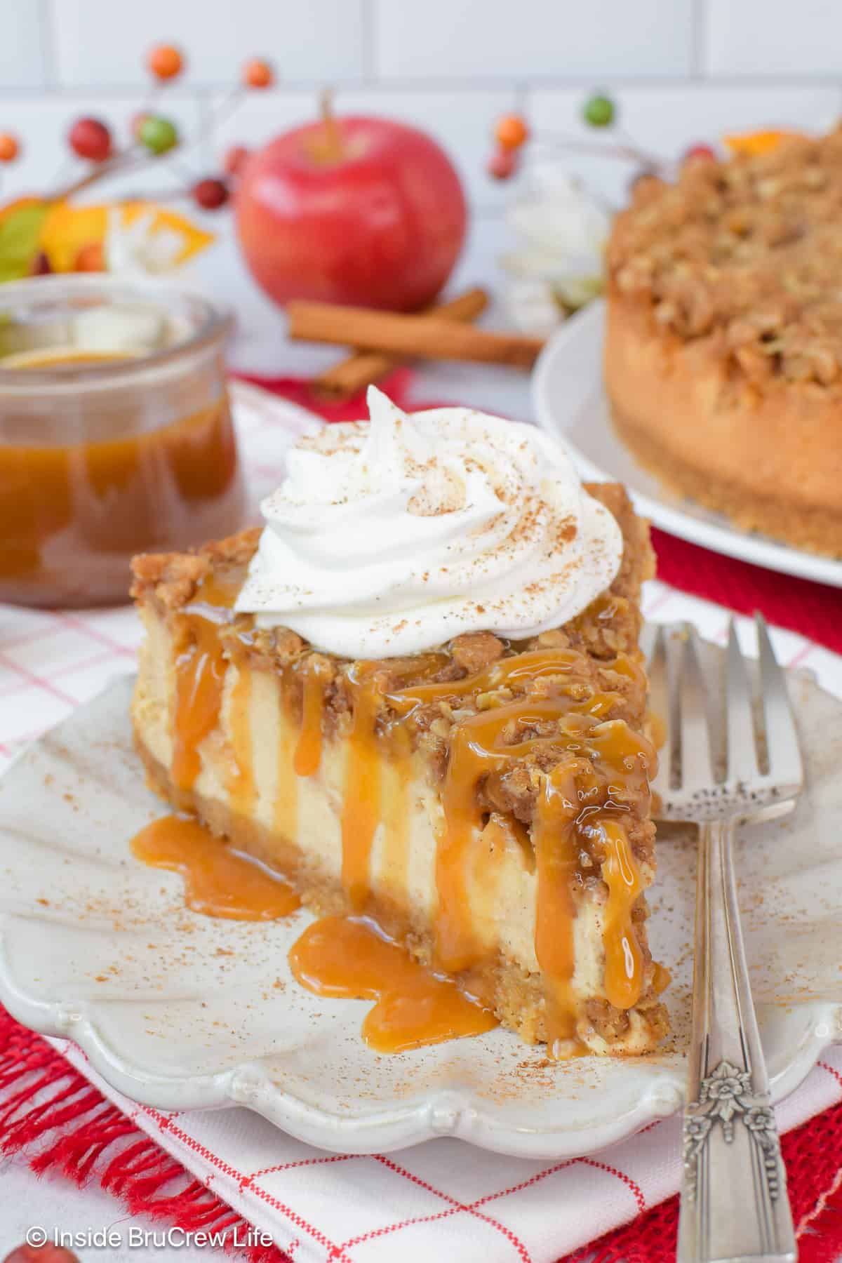 A slice of apple crisp cheesecake topped with caramel and whipped cream.
