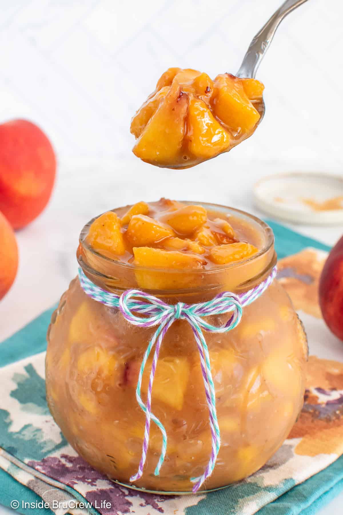A spoon lifting peach pie filling out of a jar.