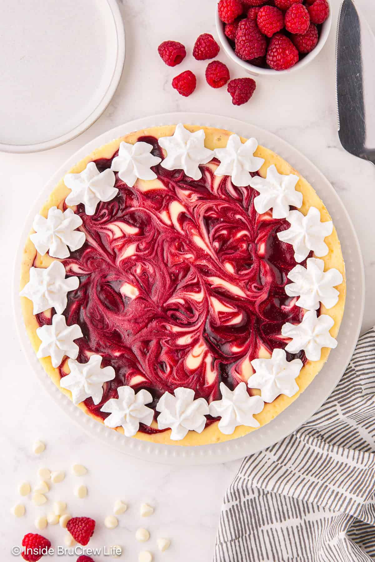 Overhead view of a white chocolate raspberry cheesecake topped with a border of piped whipped cream rosettes.