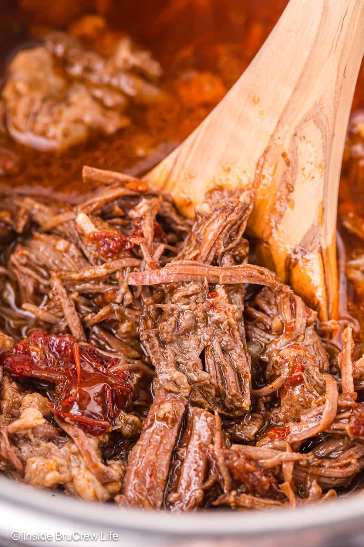 Close up of a wooden spoon stirring shredded beef barbacoa inside the Instant Pot.