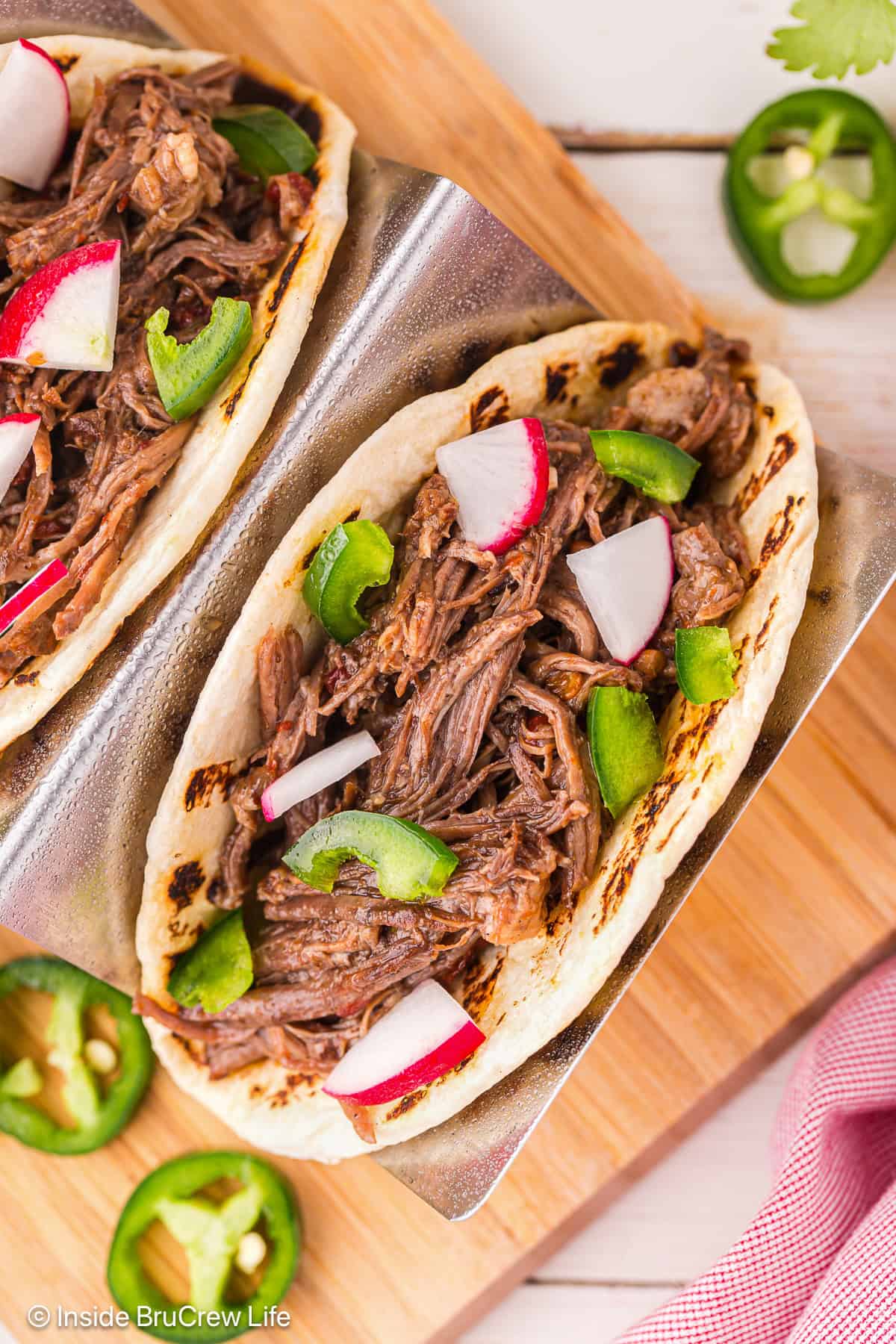 Overhead view of barbacoa tacos in a taco holder on a wooden cutting board.