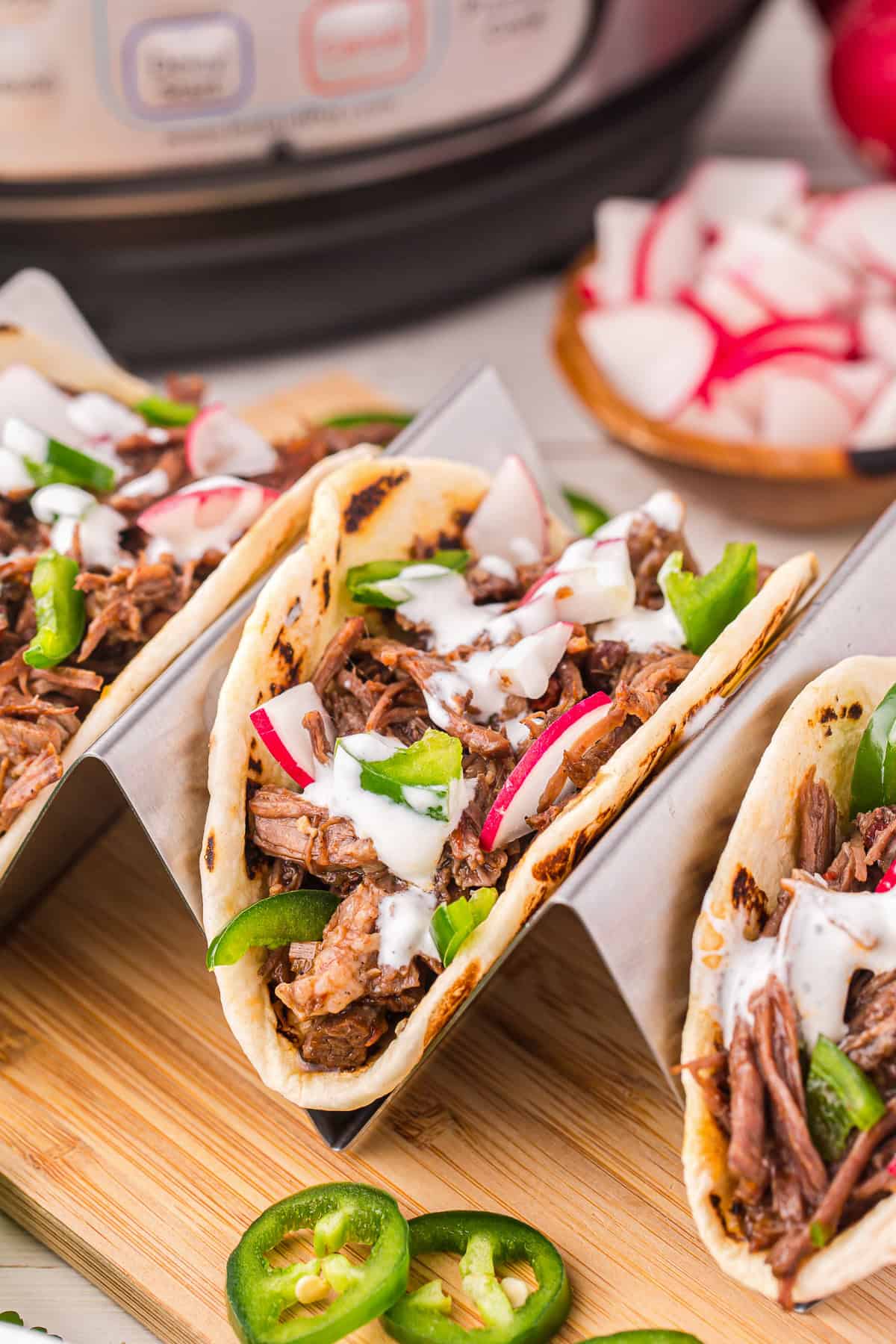 Barbacoa tacos in a taco holder on a wooden cutting board.