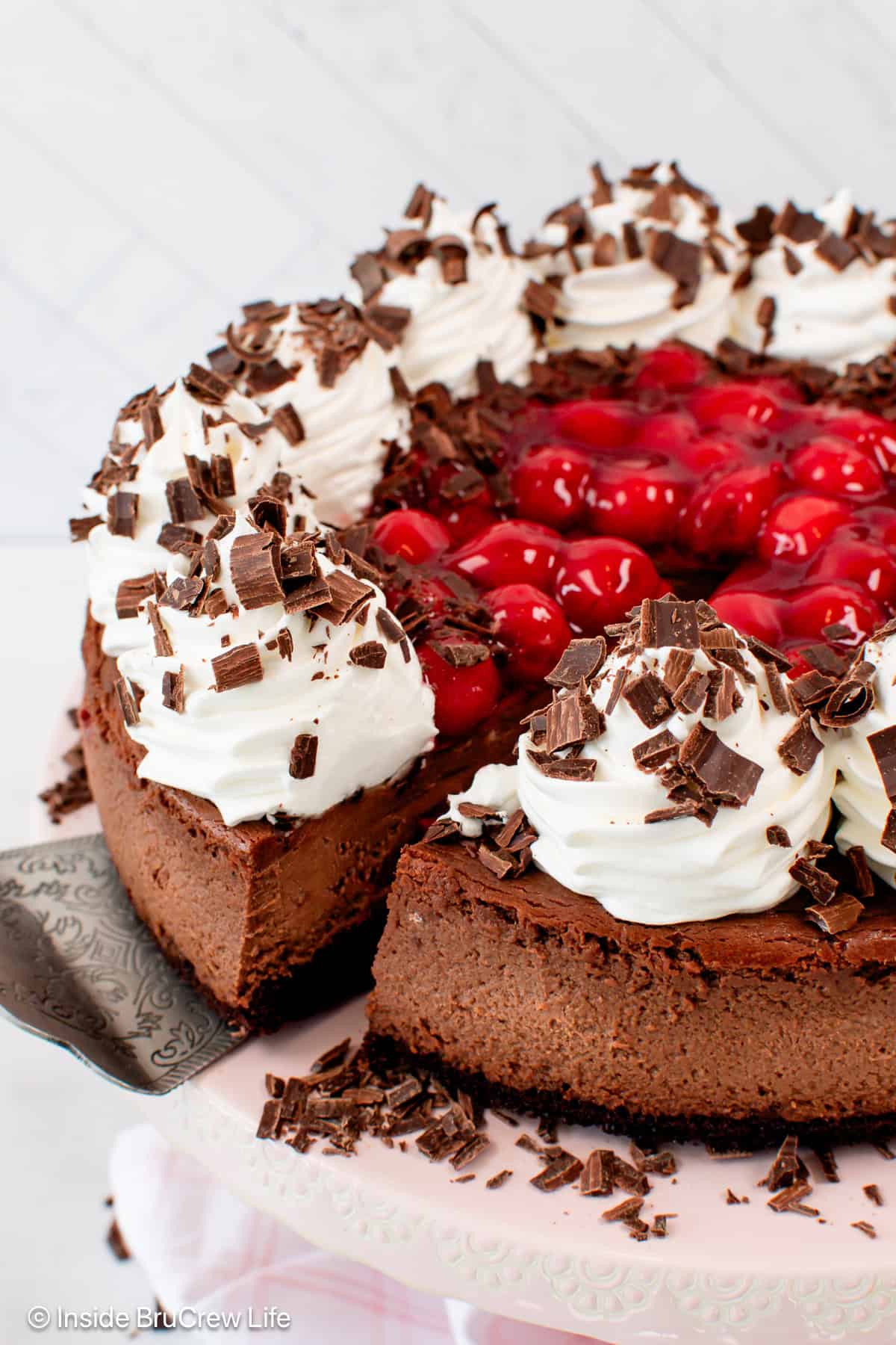 A slice of creamy black forest cheesecake partially removed from the rest of the cheesecake on a plate.