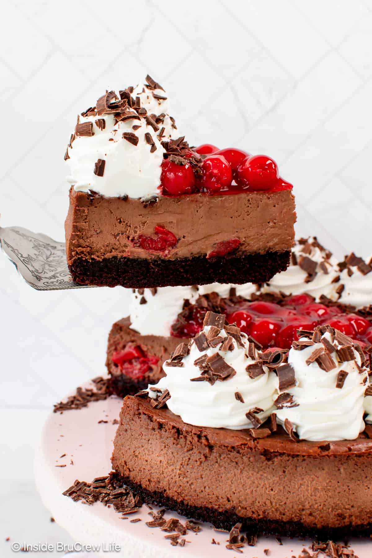 A slice of creamy black forest cheesecake being lifted from the rest of the cheesecake on a plate below.