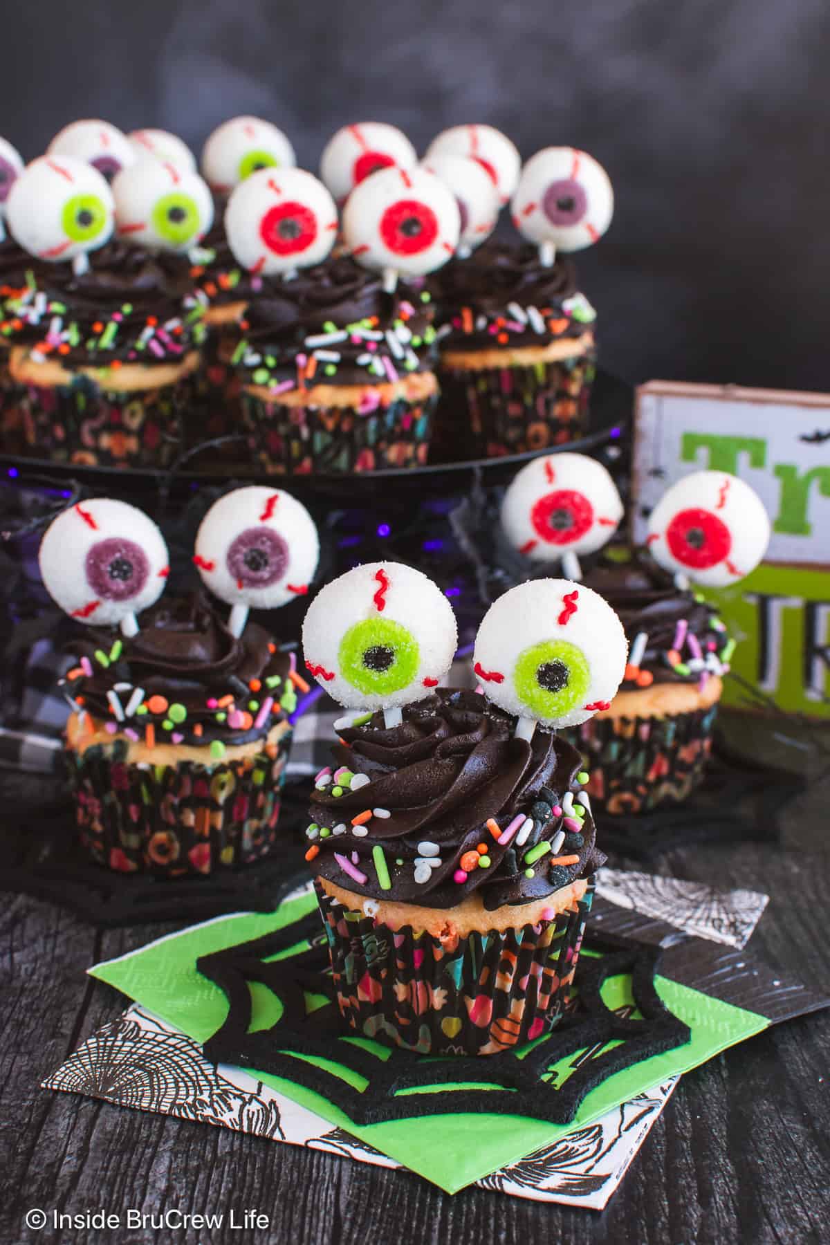 Three eyeball cupcakes with chocolate frosting and gummy eyeballs on a black board.