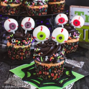 Three eyeball cupcakes with chocolate frosting and gummy eyeballs on a black board.