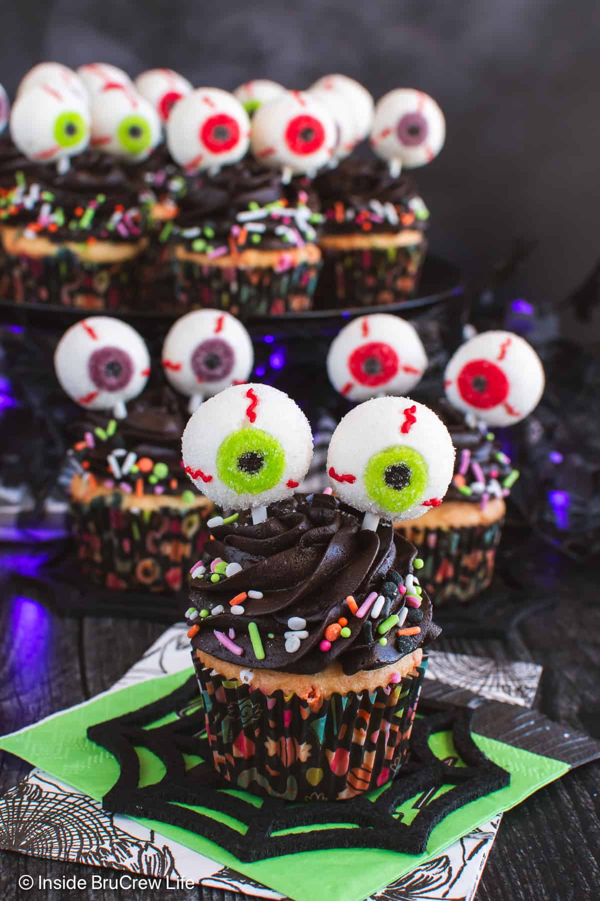 Three chocolate frosted eyeball cupcakes with sprinkles and gummy eyeballs.