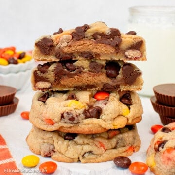 Reese's chocolate chip cookies stacked on a countertop, with the top cookie broken in half to show the gooey peanut butter cup inside.