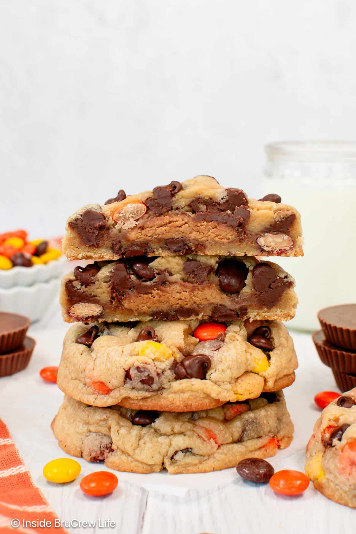 Reese's chocolate chip cookies stacked on a countertop, with the top cookie broken in half to show the gooey peanut butter cup inside.