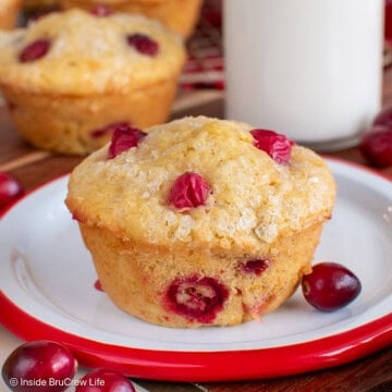 Orange muffins with cranberries on a plate and wire rack.