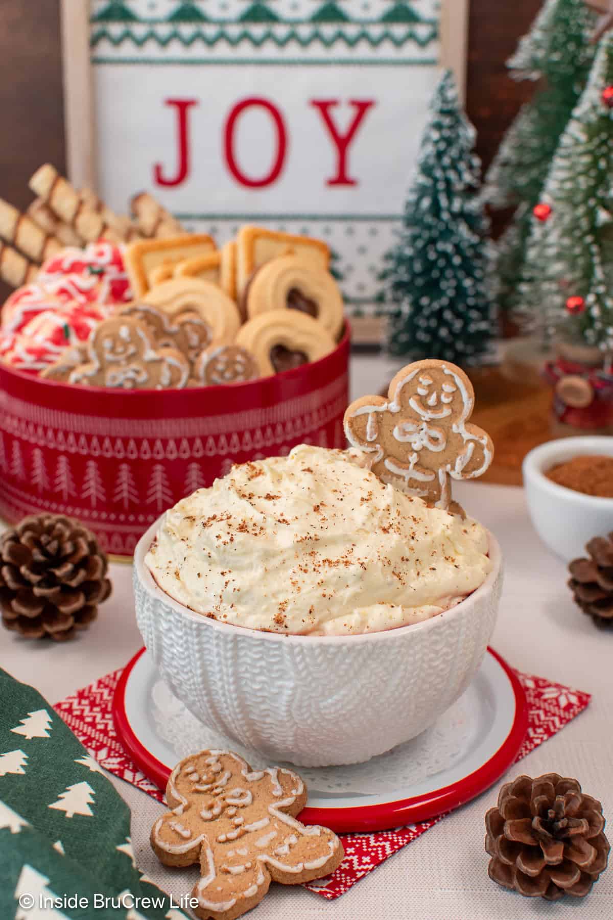 Light and fluffy eggnog dip is the easiest Christmas dessert made with instant pudding, eggnog, and whipped cream. It's ready in 10 minutes! A bowl of eggnog dip garnished with nutmeg and a gingerbread man, with a bowl of Christmas cookies and holiday decorations in the background.