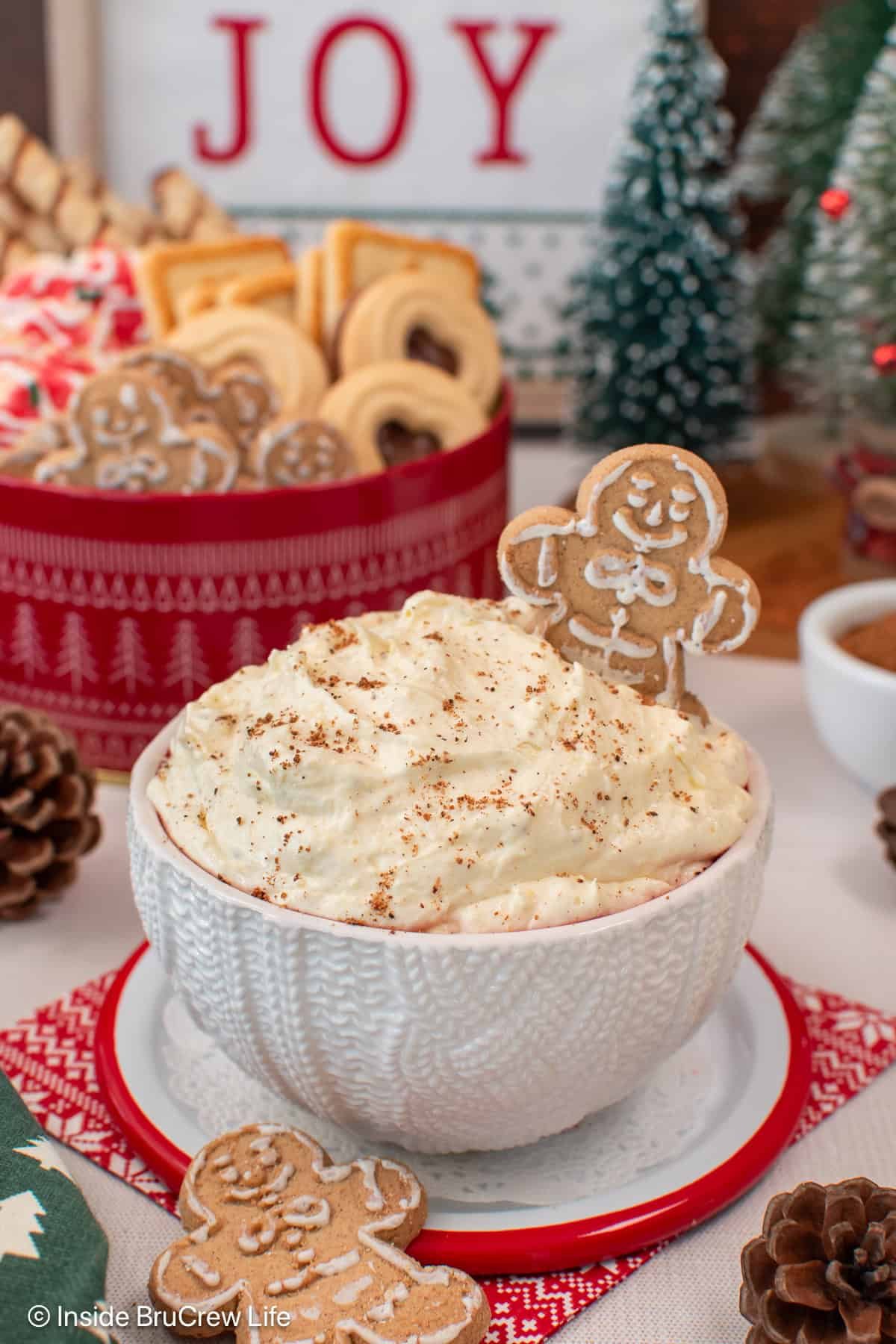 Light and fluffy eggnog dip is the easiest Christmas dessert made with instant pudding, eggnog, and whipped cream. It's ready in 10 minutes! A bowl of eggnog dip garnished with nutmeg and a gingerbread man, with a bowl of Christmas cookies and holiday decorations in the background.