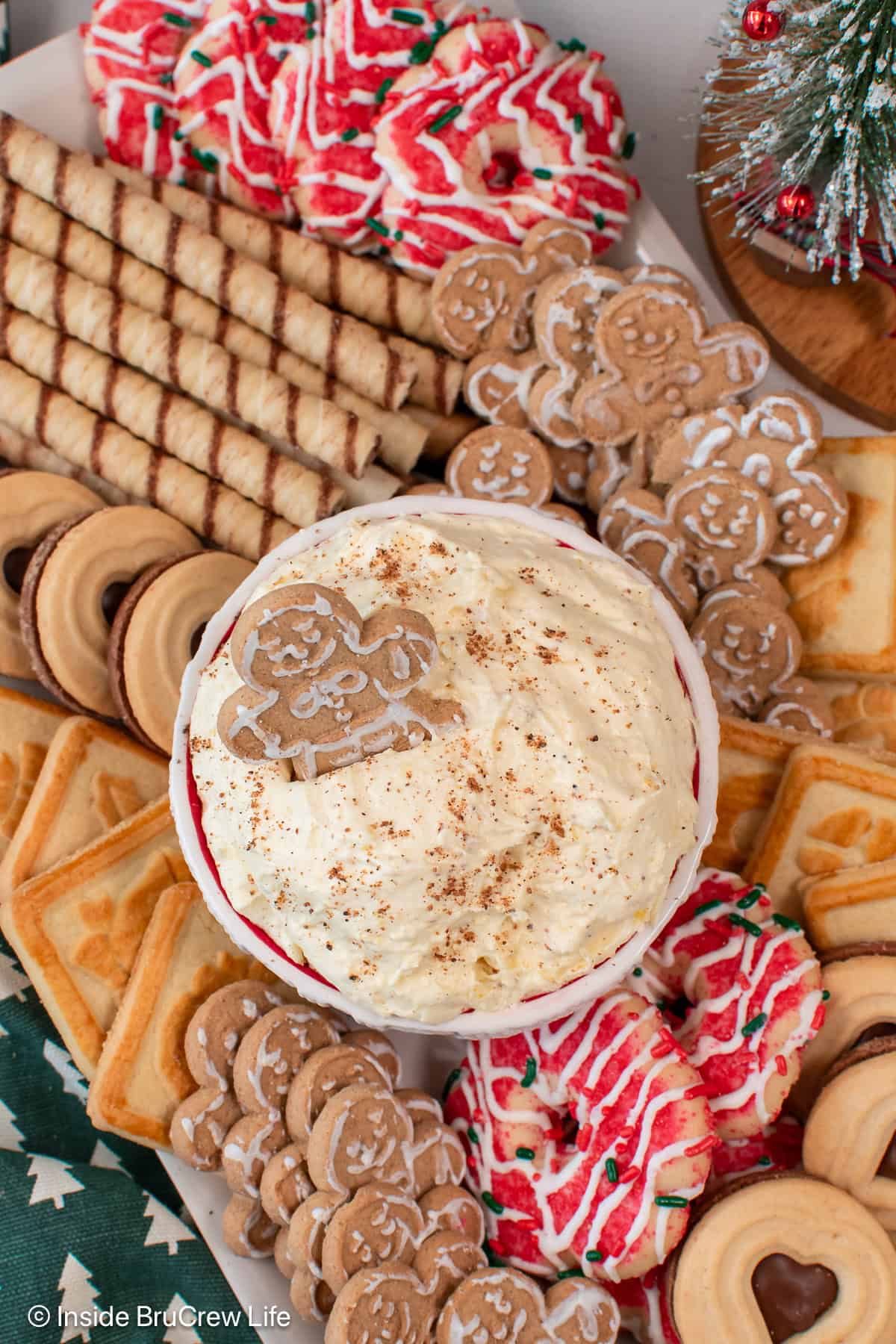 Light and fluffy eggnog dip is the easiest Christmas dessert made with instant pudding, eggnog, and whipped cream. It's ready in 10 minutes! Overhead view of a bowl of creamy eggnog dip garnished with nutmeg and a gingerbread man, surrounded by a platter of Christmas cookies.