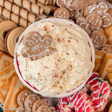 Overhead view of a bowl of creamy eggnog dip garnished with nutmeg and a gingerbread man, surrounded by a platter of Christmas cookies.