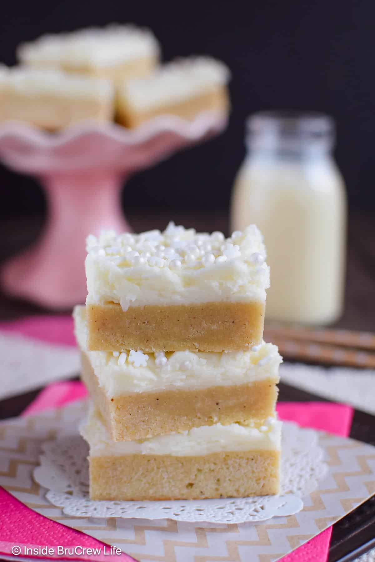 Three frosted eggnog bars stacked on a white paper.