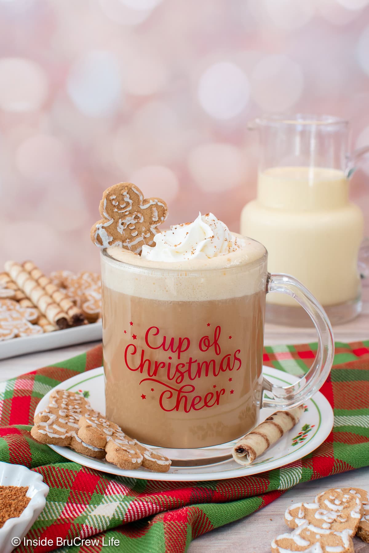 This eggnog latte recipe is rich, frothy, and easy to make at home with espresso, eggnog, and nutmeg. A cozy coffee drink for the holidays! An eggnog latte topped with a swirl of whipped cream and a mini gingerbread man in a festive mug, set on top of a red and green plaid cloth.