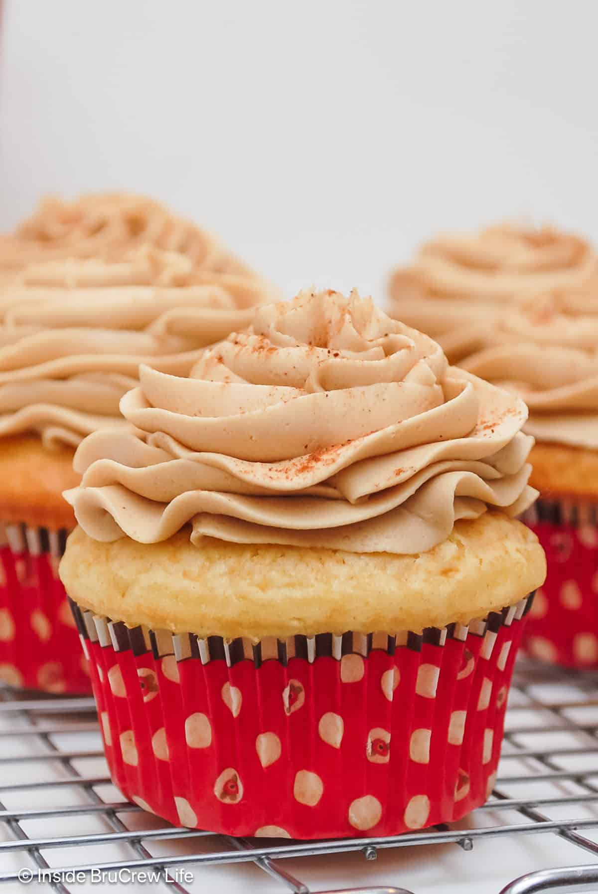 Three frosted eggnog cupcakes resting on a wire rack.