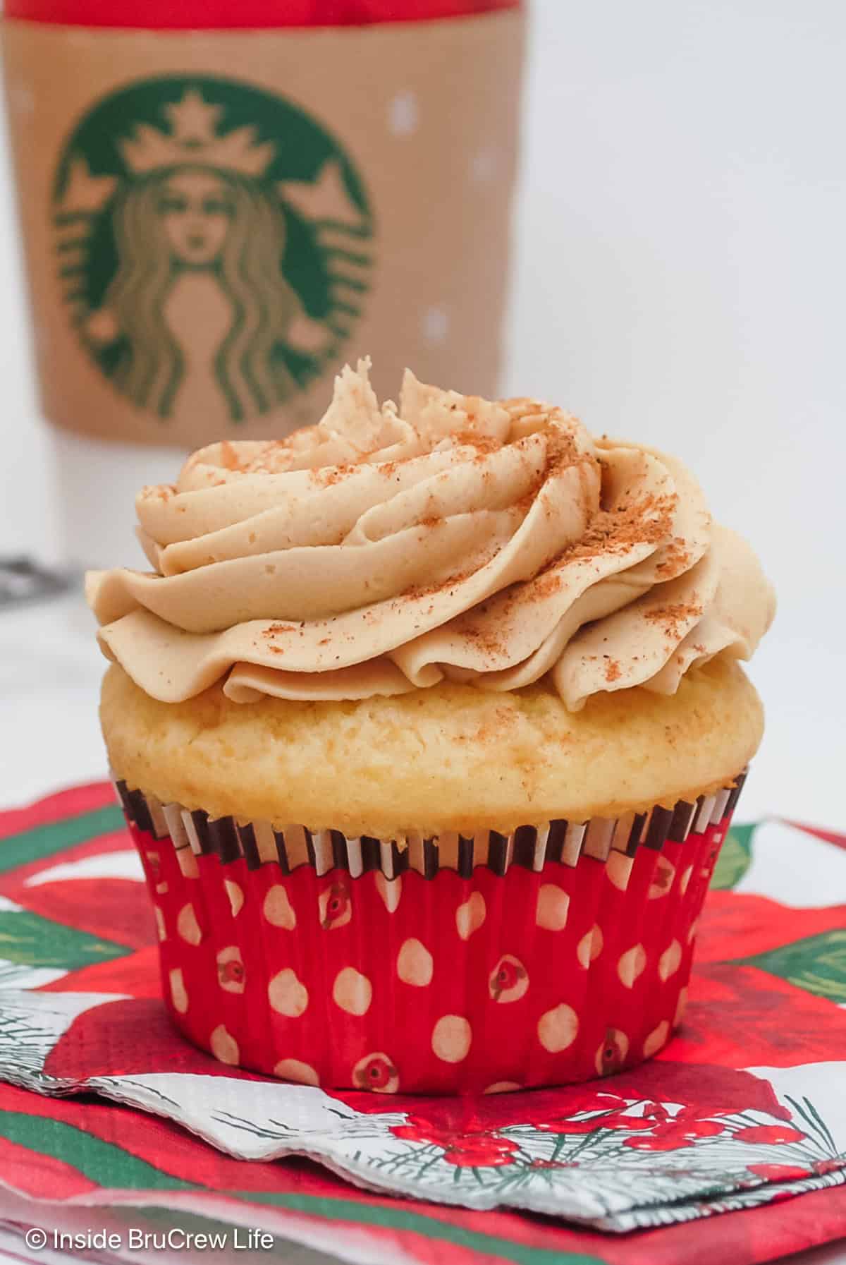 An eggnog cupcake with a swirl of coffee buttercream with a cup behind it.