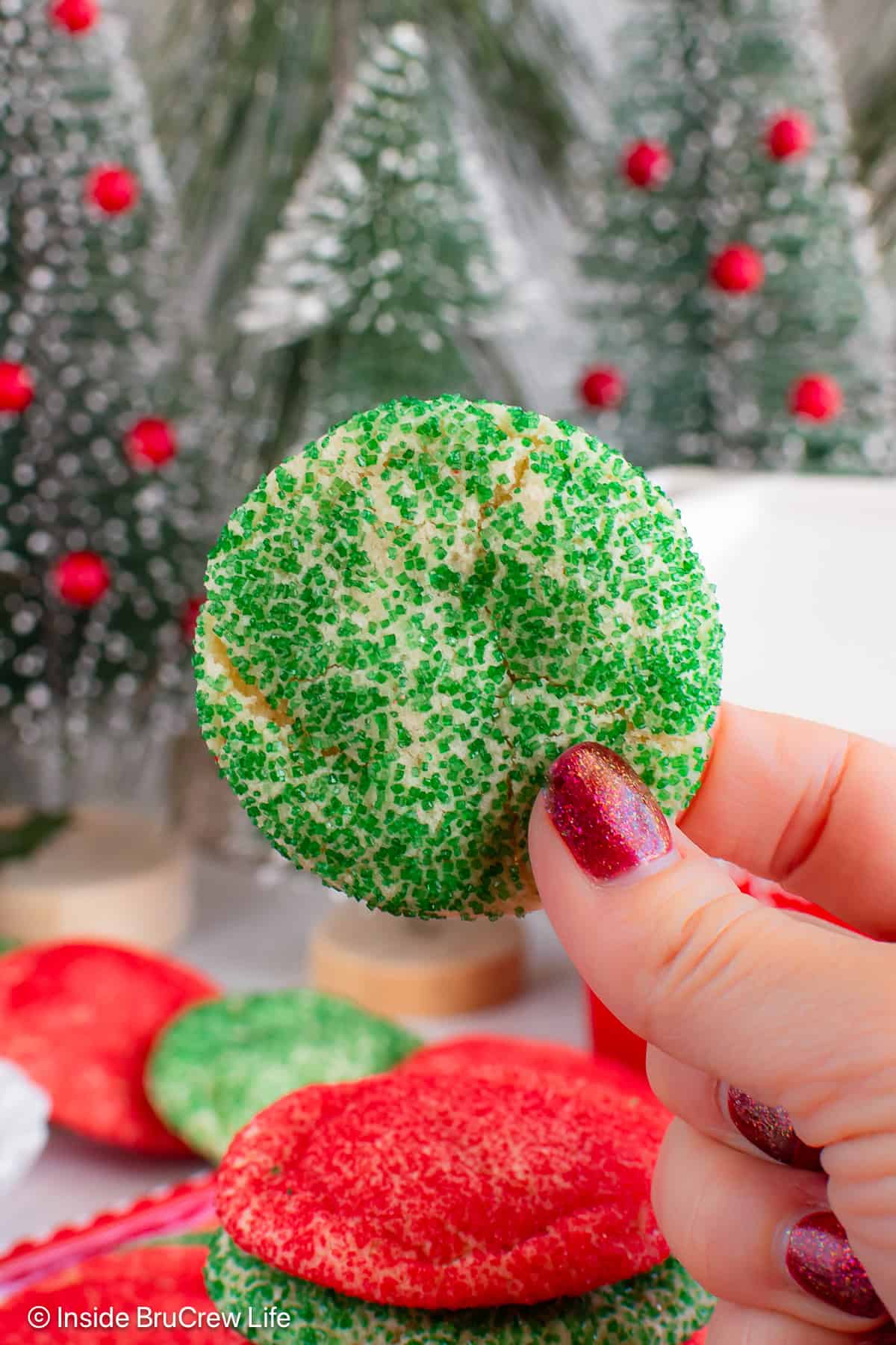 A green sugar cookie held up in the air with a hand.