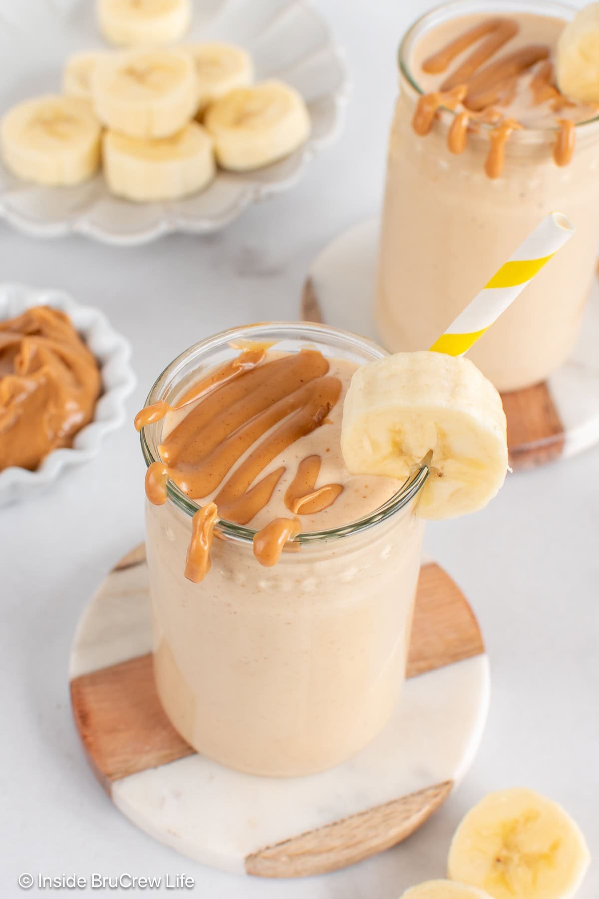 Two cups with filled with peanut butter banana smoothie and drizzled with extra peanut butter.