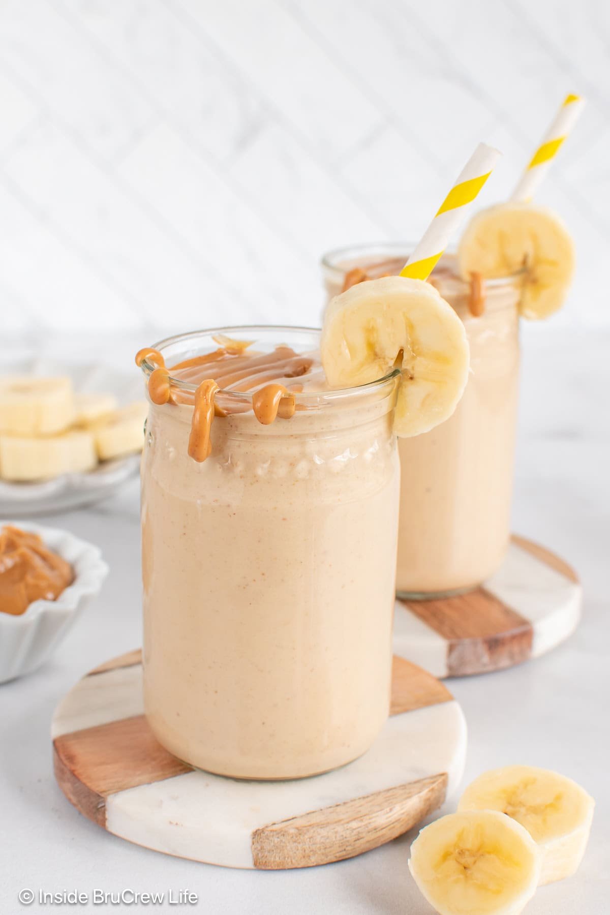 Two cups filled with a peanut butter and banana smoothie, then topped with extra peanut butter.