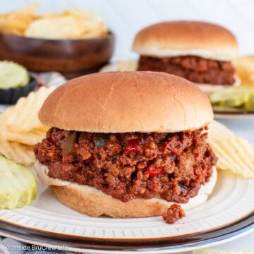 A plate with pickles, chips, and a bun filled with homemade sloppy joes.