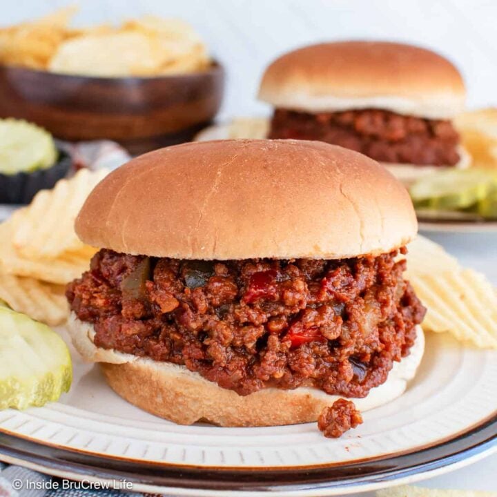 A plate with pickles, chips, and a bun filled with homemade sloppy joes.