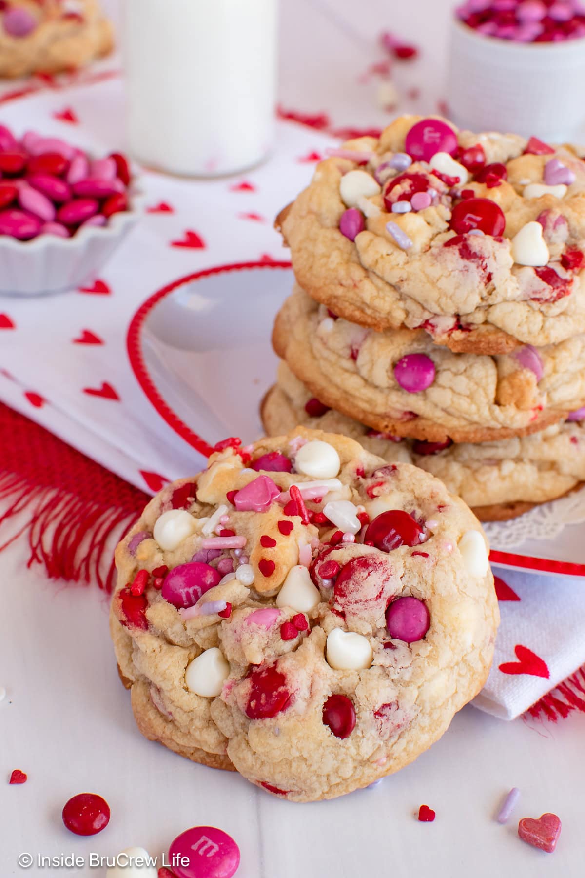 A Valentine's chocolate chip cookie propped against a plate with more cookies on it.